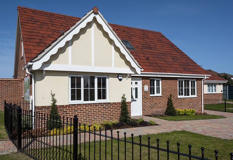 New build bungalow with blue skies, planted front garden and black metal railing fence