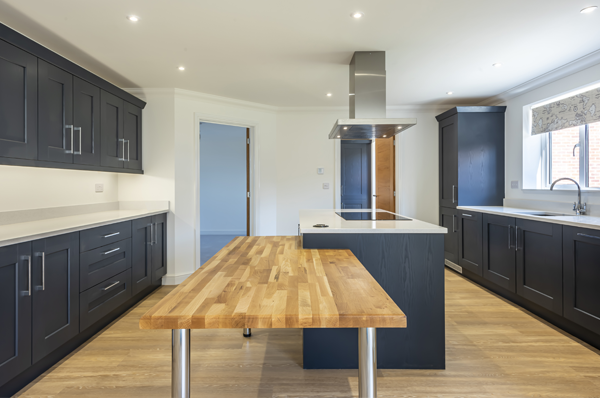 Badger Building Kitchen Photograph of open plan kitched with dark grey units, centre island, white worktops and wood laminate floor